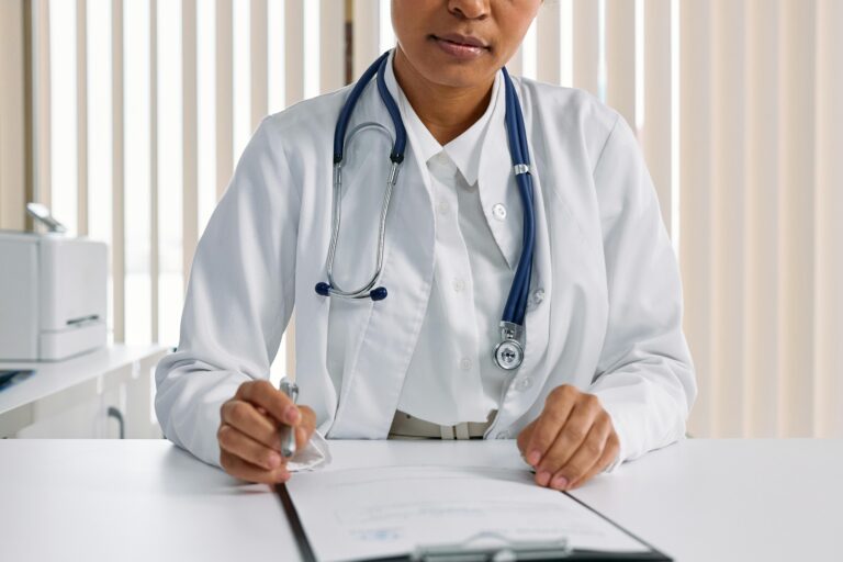 A focused doctor with stethoscope recording patient details in an office setting.